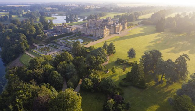 An aerial view of Blenheim Palace and the Water Terraces in early morning light, with the lake and parkland beyond
