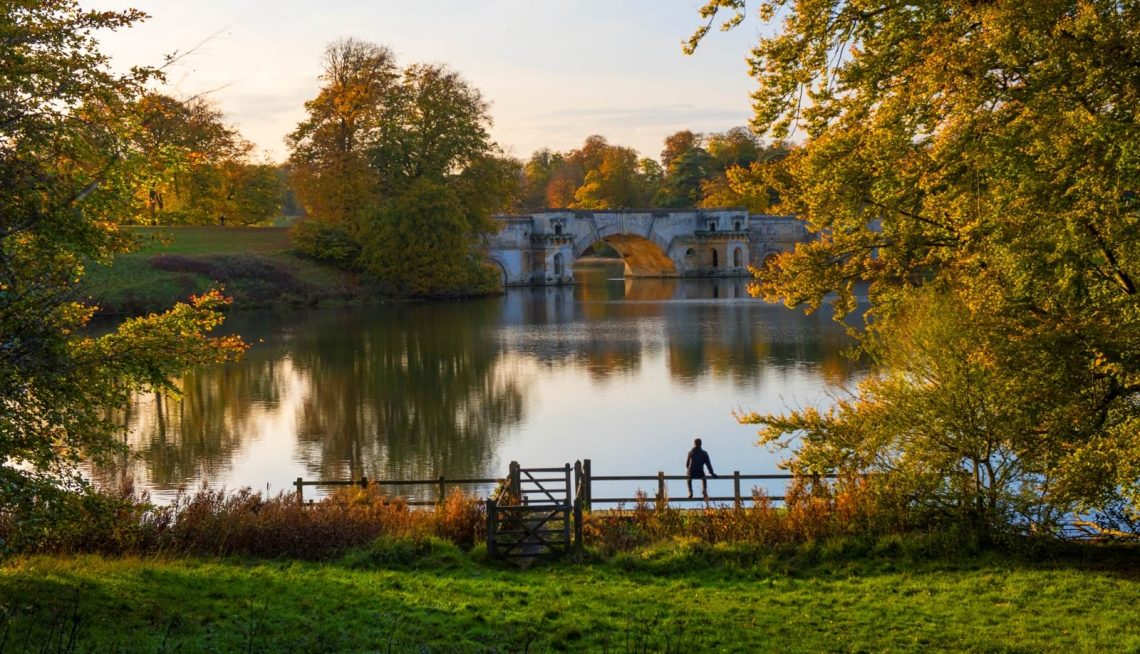 An aerial view of Blenheim Palace and the Water Terraces in early morning light, with the lake and parkland beyond