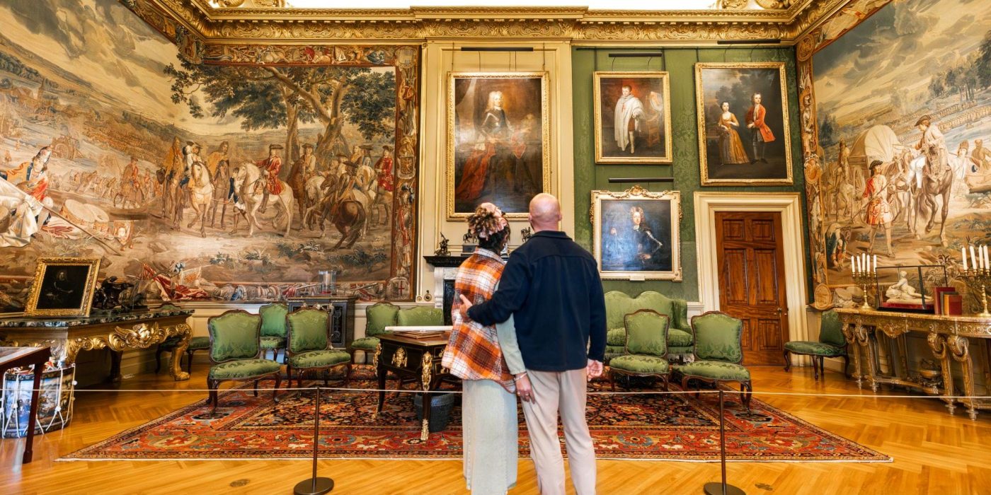 Two visitors looking at the portraits and tapestries in a green-walled State Room