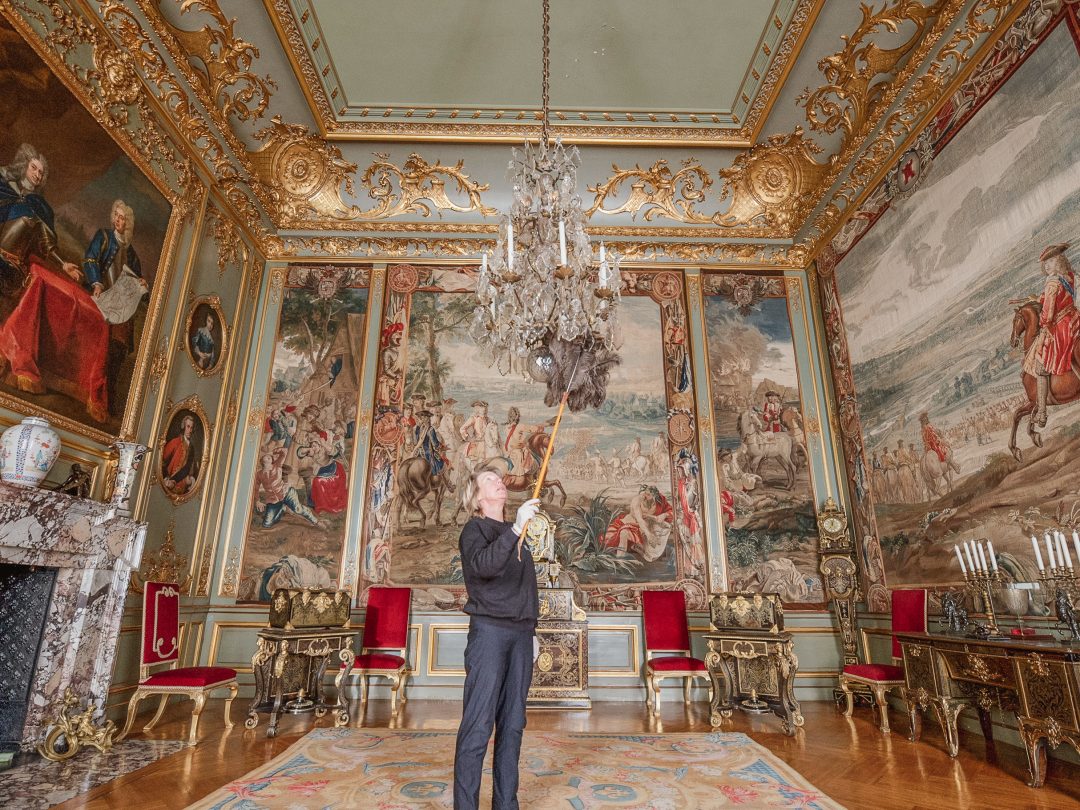 A conservator cleaning a chandelier with a long brush in one of the State Rooms