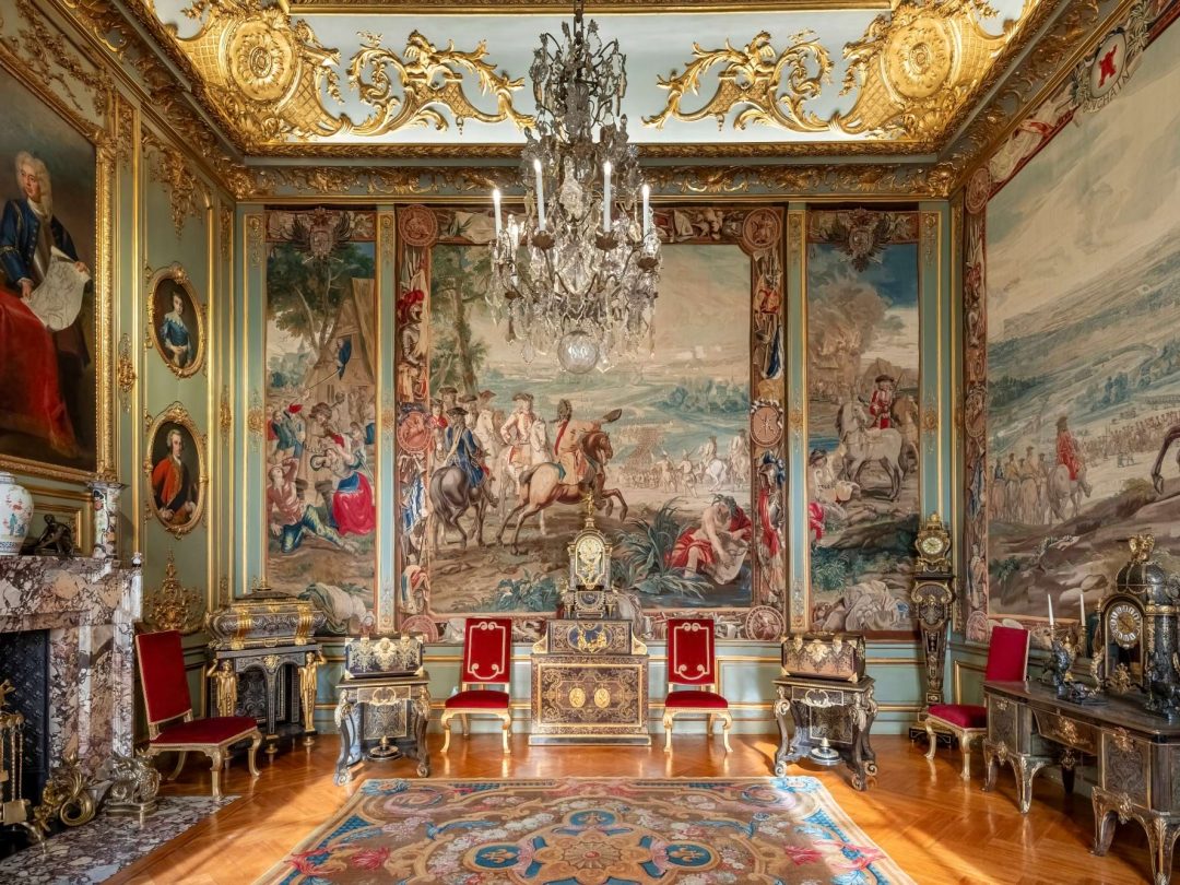 A State Room hung with the Marlborough tapestries, with gilt and red chairs beneath a chandelier