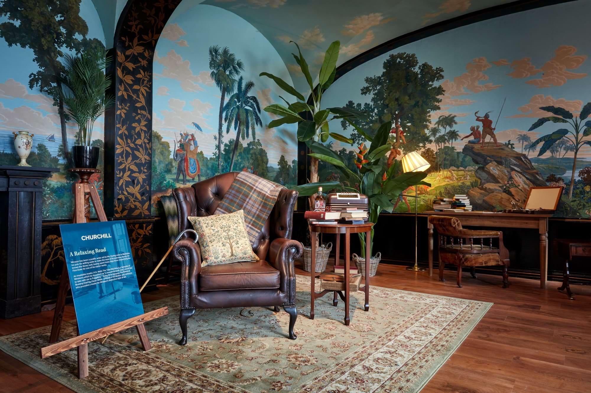 A leather armchair, books and a lamp set against painted mural walls in the Churchill exhibition