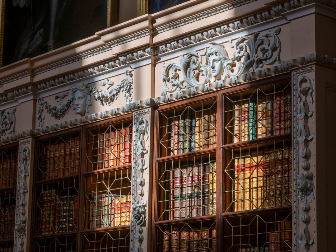 Stucco masks and swags above the gilded book spines in the Long Library bookcases