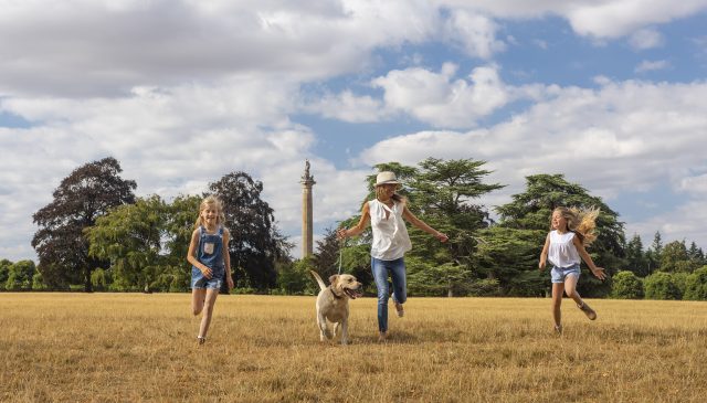 A family running across the park with their dog, the Column of Victory behind them