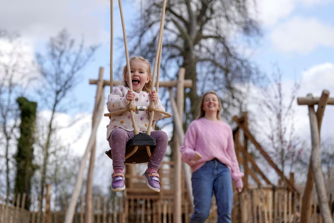 A young girl laughing on a swing while a woman watches