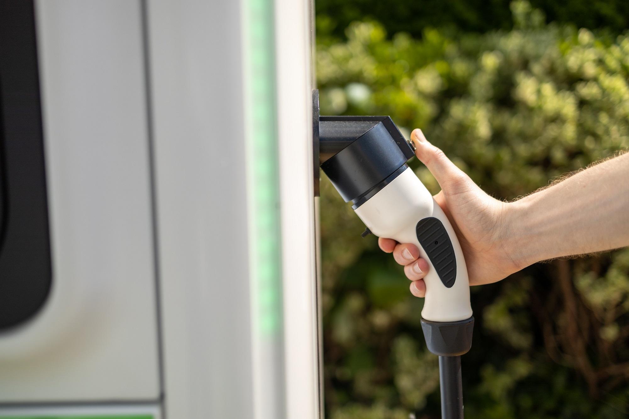 A hand holding an electric vehicle charging connector at a charge point