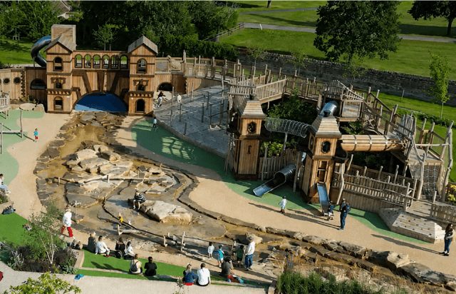 Families on the wooden fort, slides and water play area at Blenheim Palace Adventure Play, seen from above