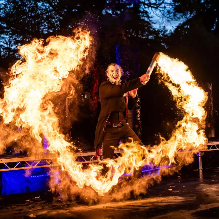 Fire performer in an Egyptian-style gold costume spinning a flaming staff at night, with costumed performers behind