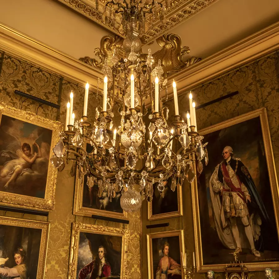 A candlelit crystal chandelier in a gilded state room hung with portraits
