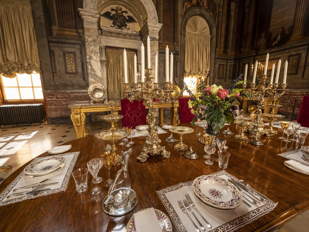 The Saloon laid for dinner with gilt candelabra and gold plate beneath its painted walls