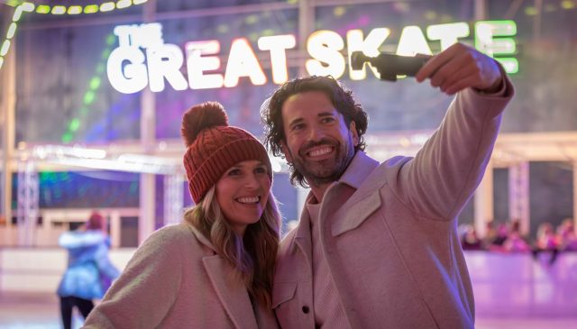 A couple taking a selfie at the ice rink beneath a Great Skate sign
