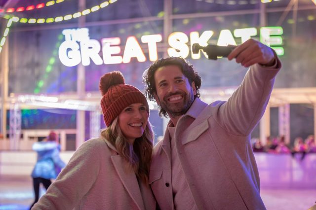 A couple taking a selfie at the ice rink beneath a Great Skate sign