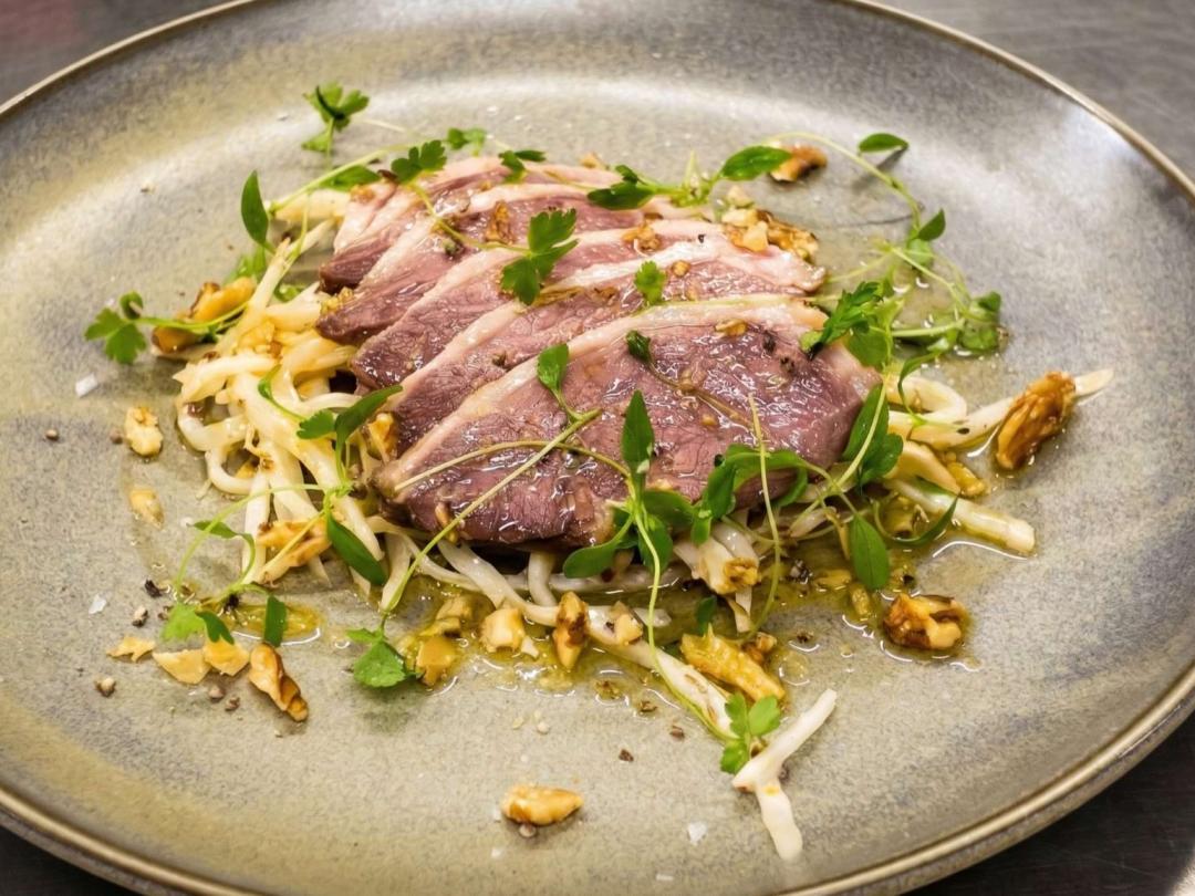 A plated dish of sliced duck breast with celeriac, walnuts and herbs