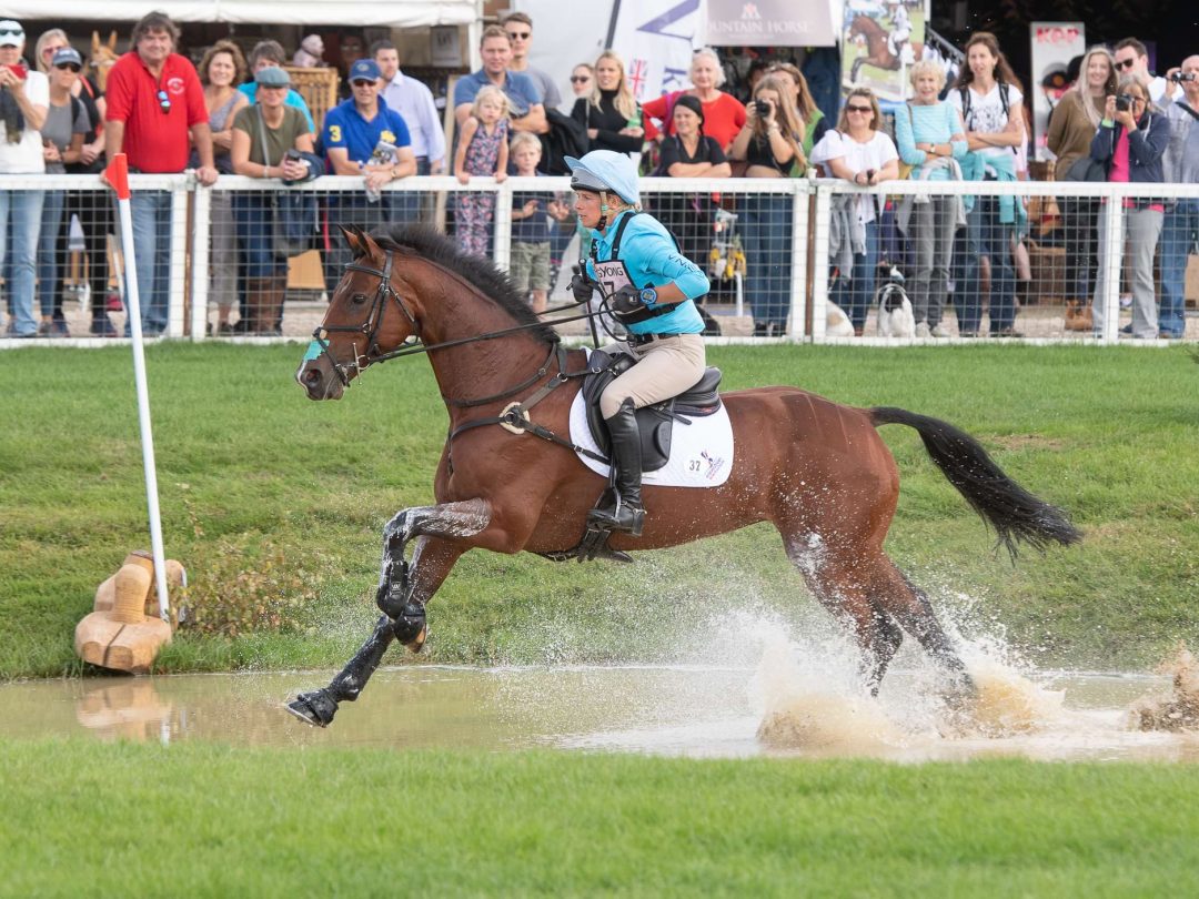 A rider and horse galloping through the water jump at the horse trials, watched by spectators
