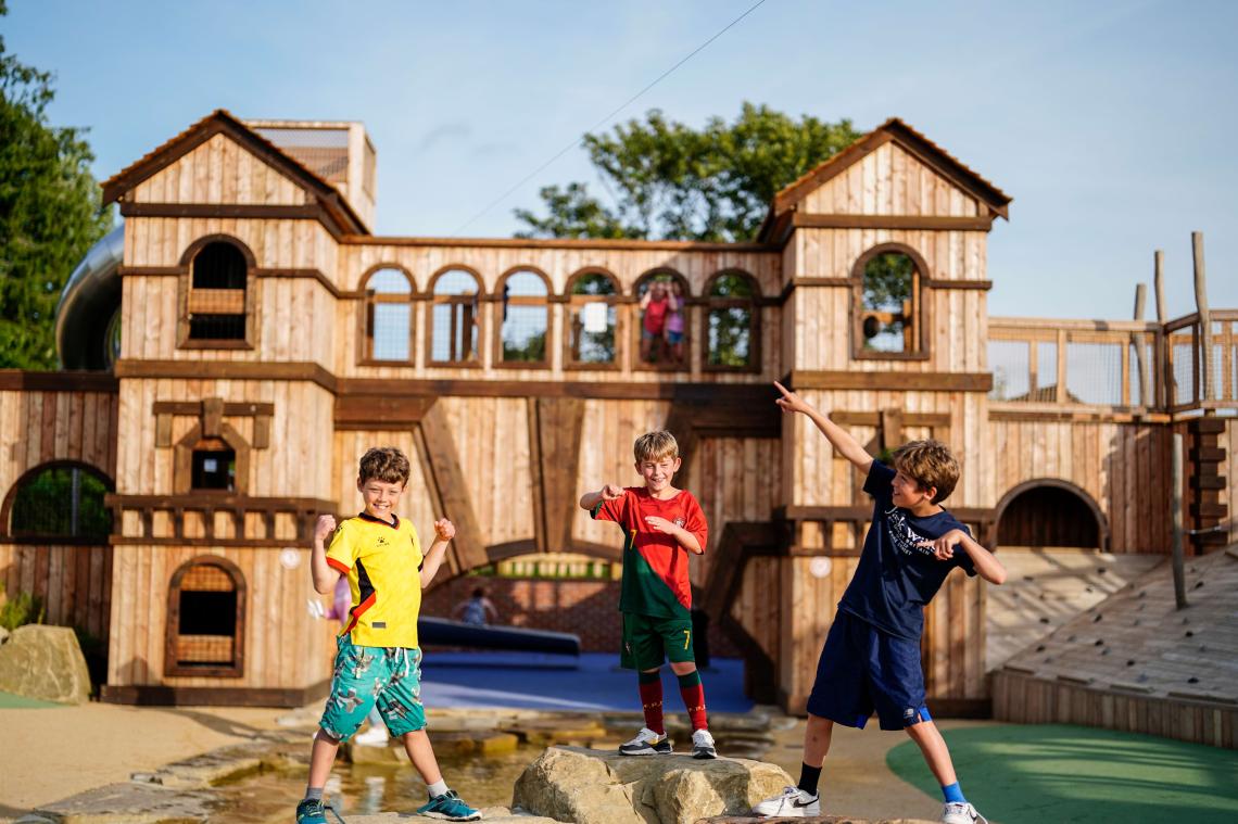Three children playing on the wooden fort in the adventure playground