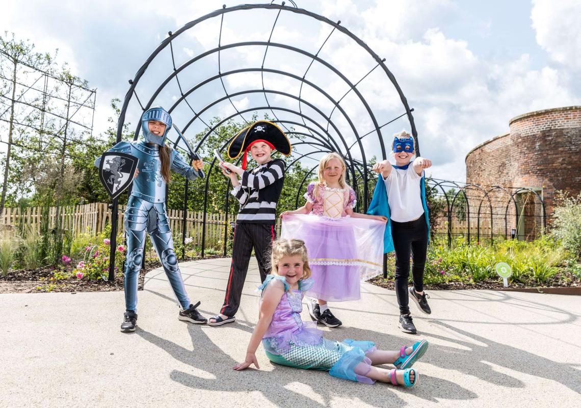 Children in fancy dress beneath a metal arch in the walled garden