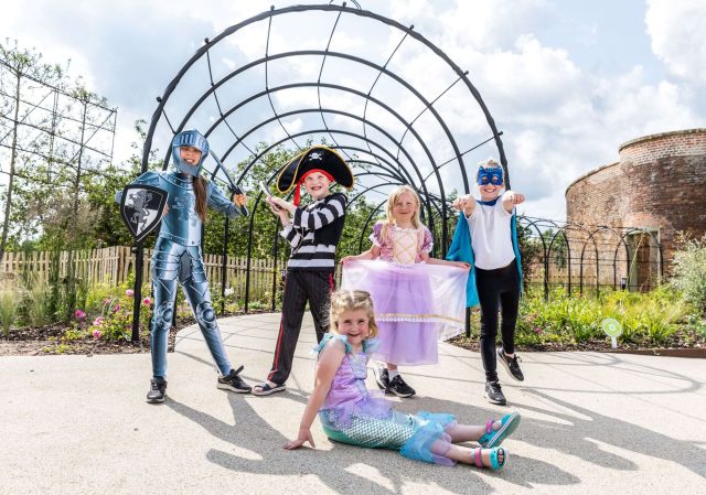 Children in fancy dress beneath a metal arch in the walled garden