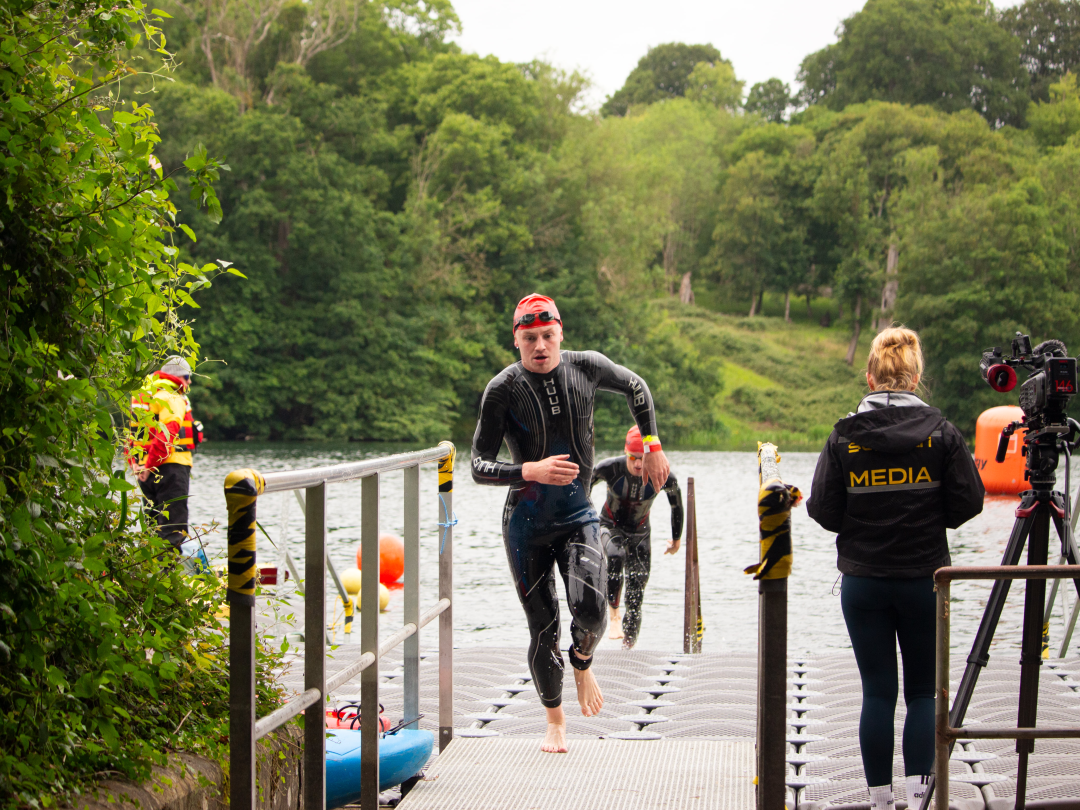 A triathlete running from the lake onto the pontoon at the swim exit