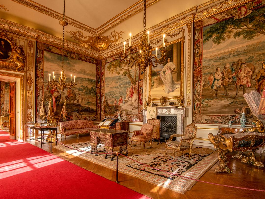 A State Room hung with tapestries and lit by candle chandeliers, with a red carpet runner through the doorways