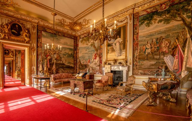 A State Room hung with tapestries and lit by candle chandeliers, with a red carpet runner through the doorways