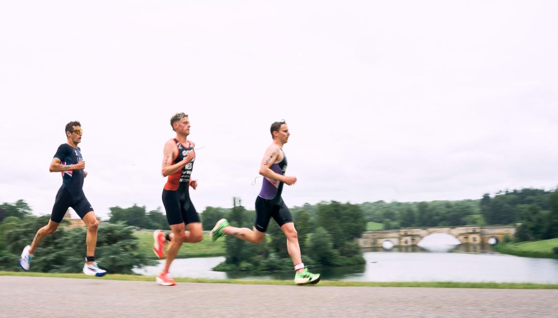 Three triathletes running beside the lake with the Grand Bridge behind