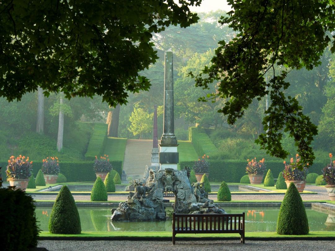 The lower Water Terrace with its obelisk fountain, clipped topiary and a bench in morning light