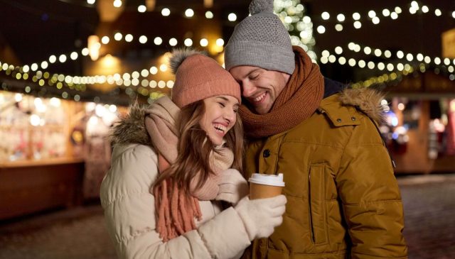 A couple with hot drinks among the lights of a Christmas market