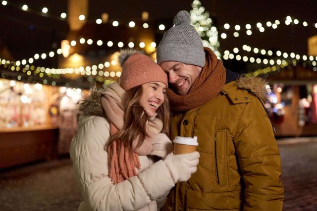 A couple with hot drinks among the lights of a Christmas market