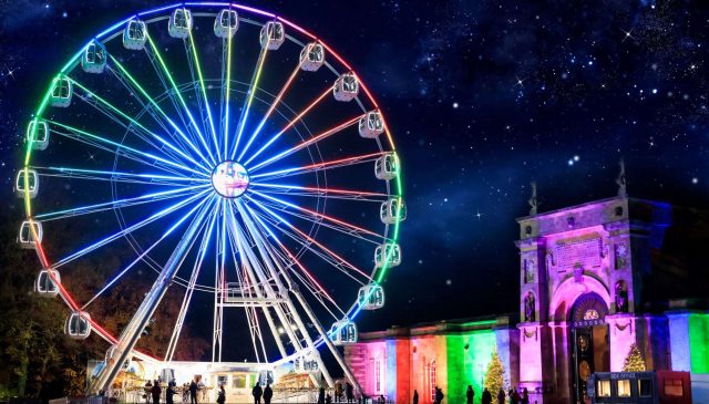 A brightly lit observation wheel at night beside the illuminated Palace gateway