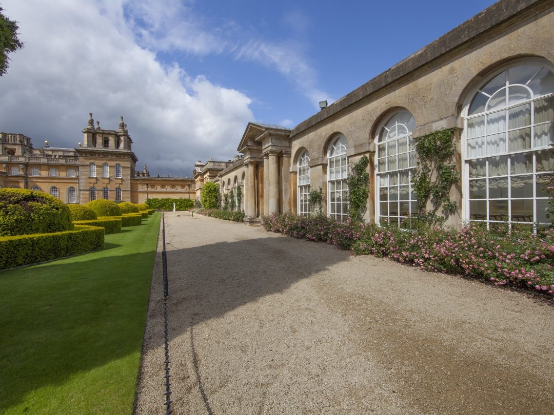 The gravel path beside the arched windows of the Orangery, with roses in bloom and the Palace beyond