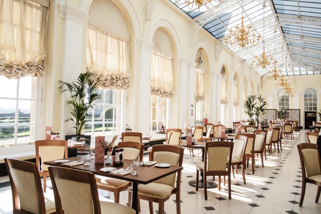 The Orangery restaurant beneath its glass roof, with tables laid and chandeliers above