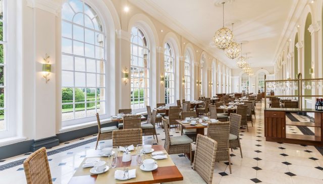 Tables laid in the Orangery restaurant beneath tall arched windows and globe chandeliers