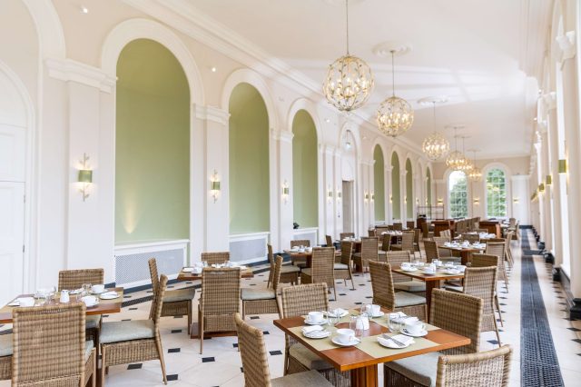 The Orangery restaurant laid for service, with green alcoves and globe chandeliers