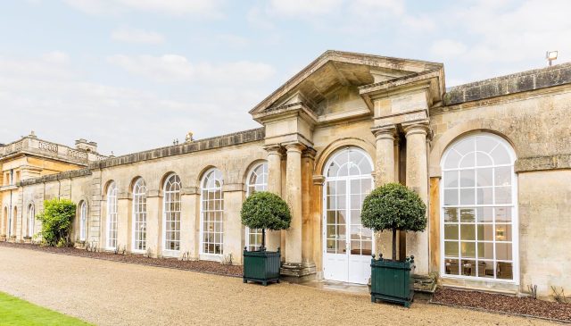 The exterior of the Orangery restaurant, with tall arched windows and clipped bay trees beside the door