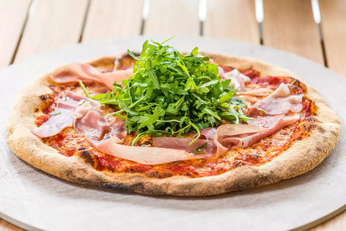 A stone-baked pizza topped with cured ham and rocket