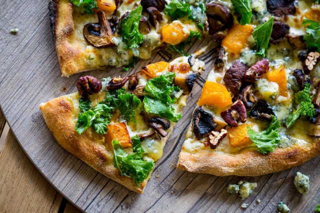 A pizza topped with squash, mushrooms, kale, blue cheese and pecans on a wooden board