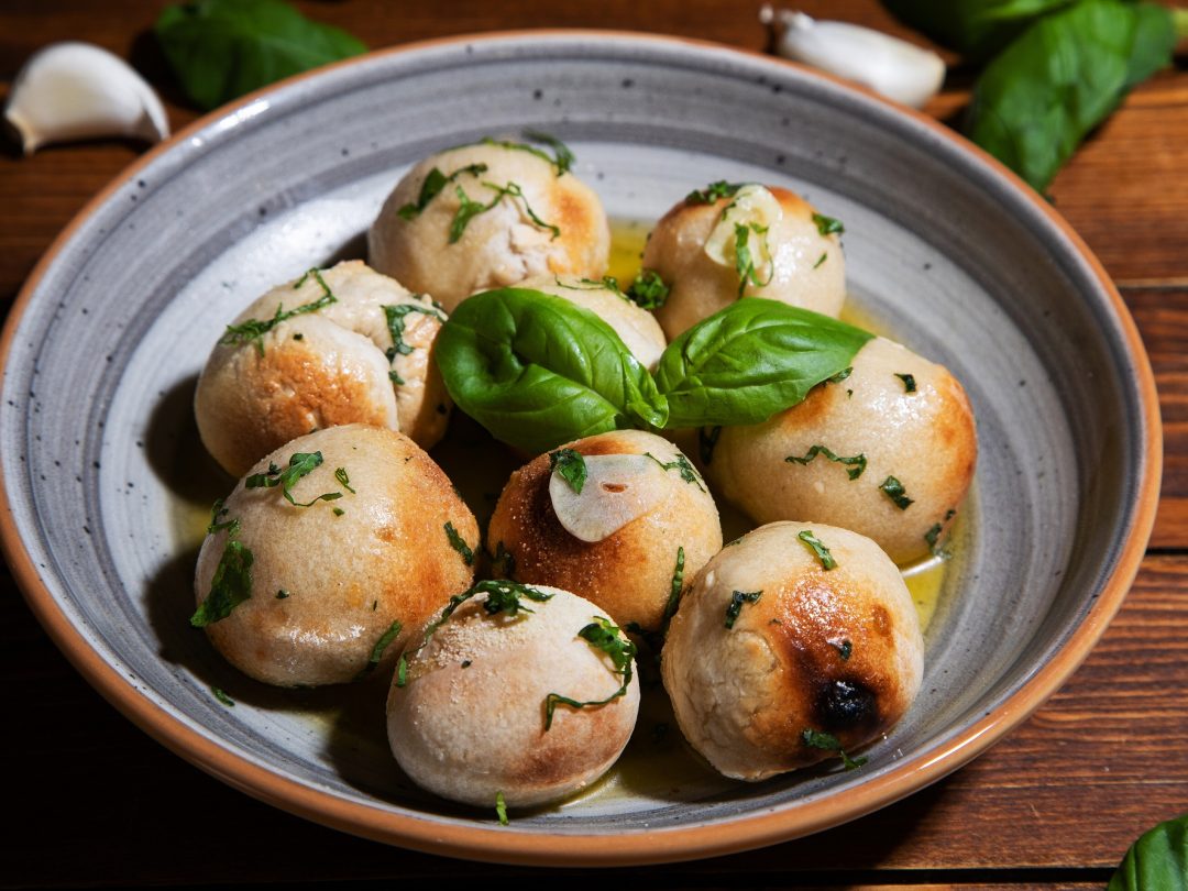 A bowl of baked dough balls in garlic butter with herbs and basil