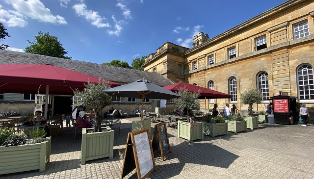 Outdoor tables with red parasols and menu boards in the courtyard outside the Stables Cafe