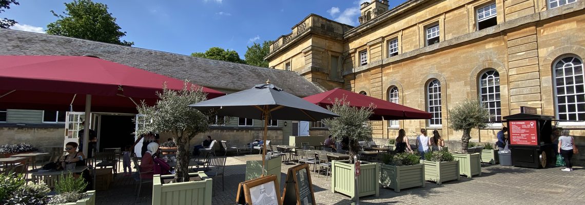 Outdoor tables with red parasols and menu boards in the courtyard outside the Stables Cafe