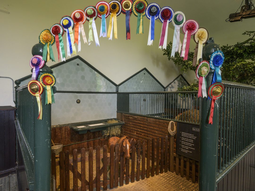 An arch of prize rosettes above a stable stall display in the stables exhibition