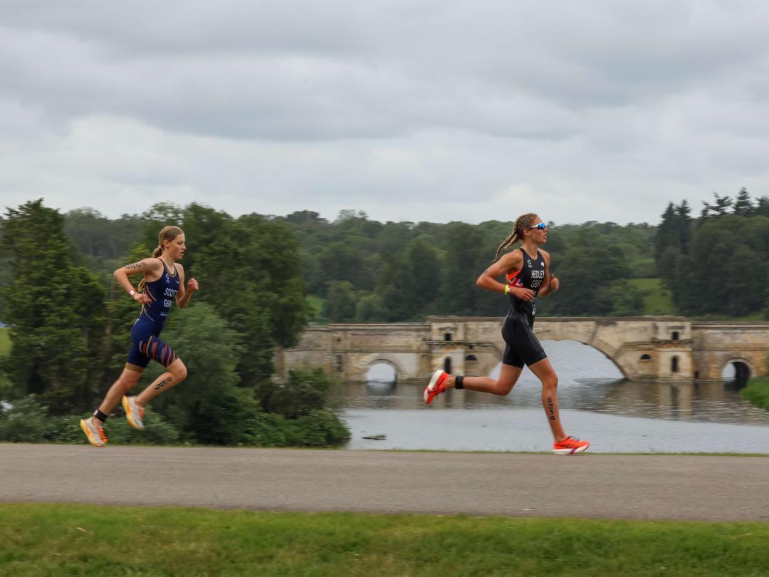 Two triathletes running beside the lake with the Grand Bridge behind them