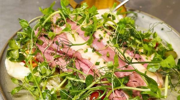 A plate of sliced rare beef dressed with pea shoots and herbs