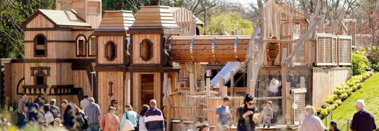 Families walking past the wooden play towers of Adventure Play on a sunny day