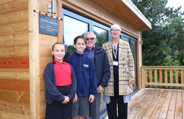 A girl, a boy, an older man and a woman stand together on the deck of a new wooden building
