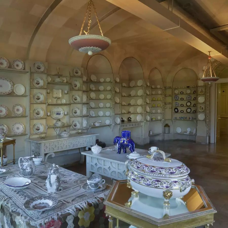 The china room, a vaulted room lined with shelves of plates, with tureens and a blue elephant