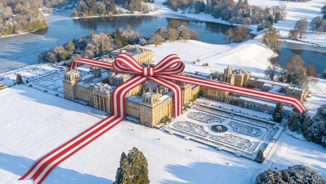 Aerial view of the Palace and formal gardens in snow, wrapped in a giant red and white striped ribbon and bow, with the lake beyond