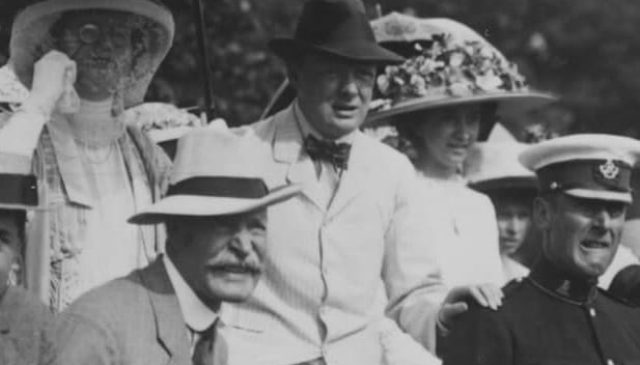 Black and white archive photograph of a crowd in summer hats and suits, with a uniformed officer