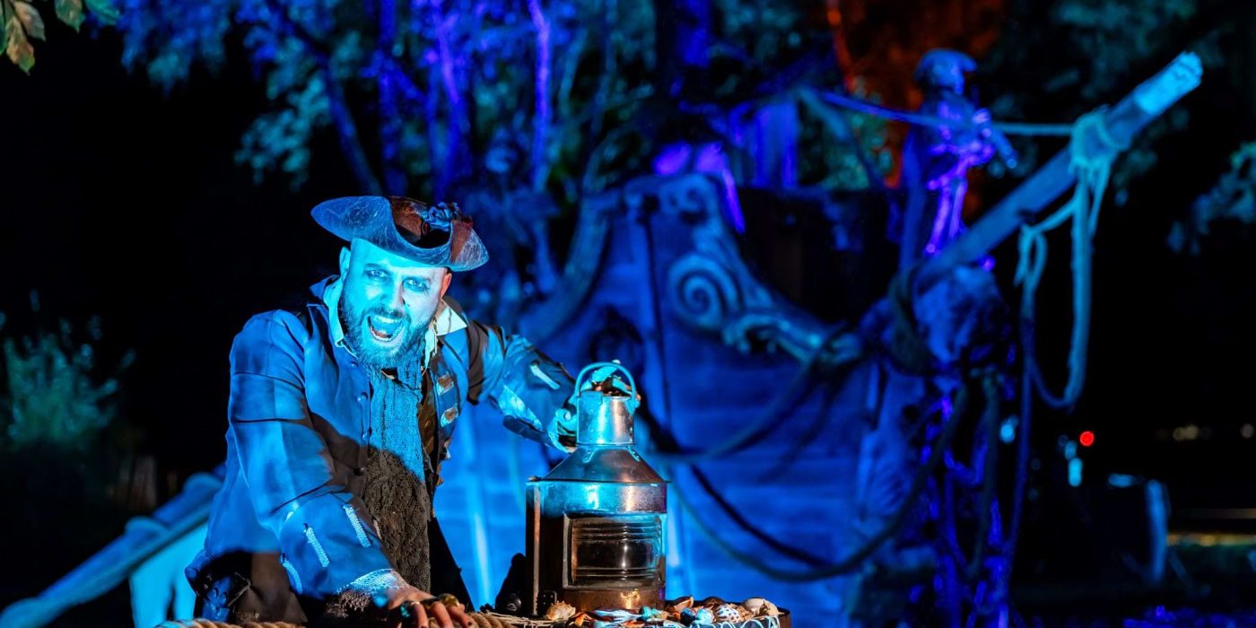 A scarecrow above a wooden crate of pumpkins, with carved jack-o'-lanterns on the grass at night