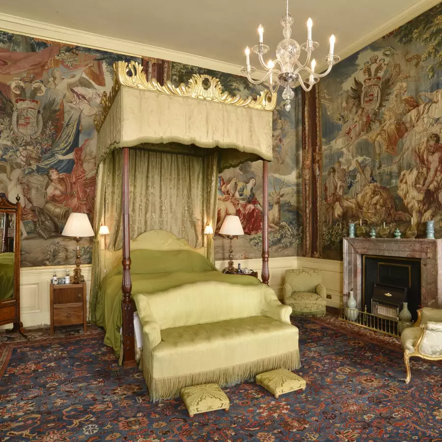 A canopied four-poster bed and a sofa in a tapestry-hung bedroom with a chandelier