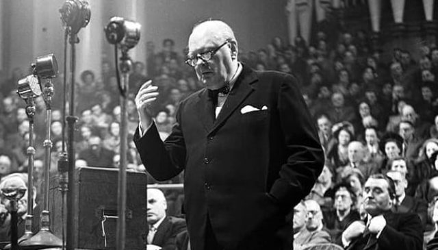 Sir Winston Churchill speaking at a bank of microphones before an audience